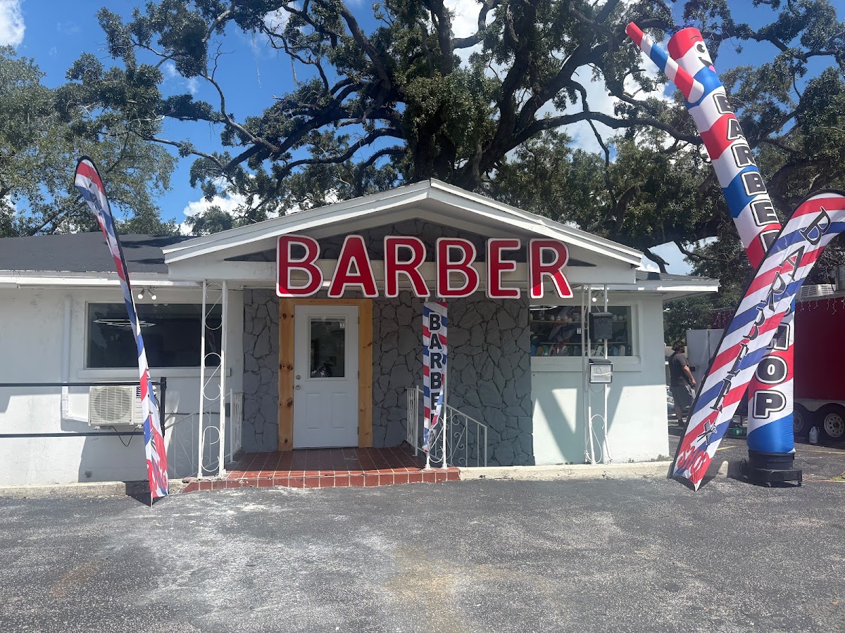 Exterior of Juan Elegant Barbershop with a large red BARBER sign and barber flags